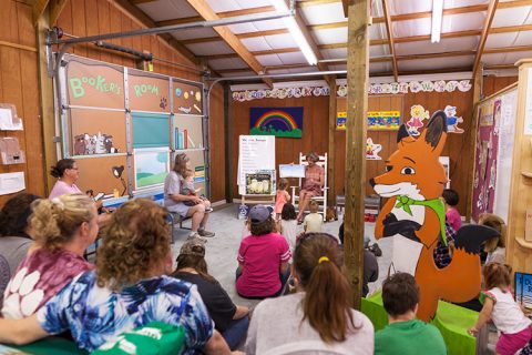 A group of children and adults sit in a circle at Adventure Tales story time at Green Valley Book Fair.